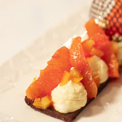 Image montrant le dessert "L'Oie-soffee" du restaurant Les Oies Sauvages. Un biscuit crumble aux écorces d’oranges confites et ganache chocolat noir, une crème princesse au kalamansi et ses suprême d’orange sanguine délicatement disposés sur le dessus